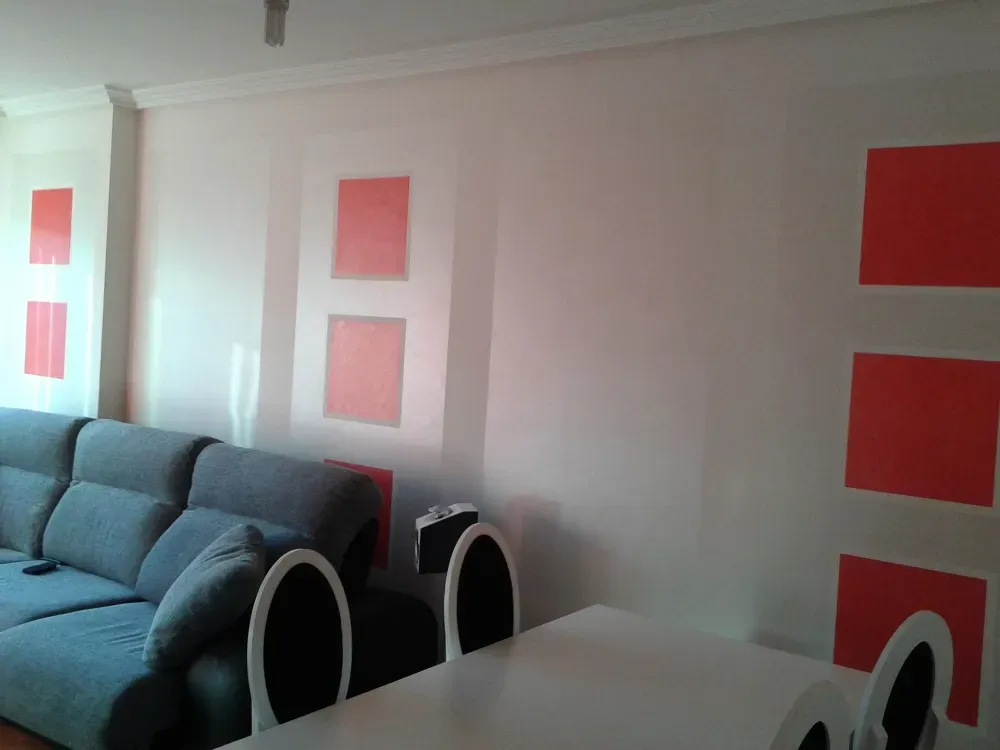 Interior de sala de estar con paredes blancas, cuadrados rojos y sofá azul.