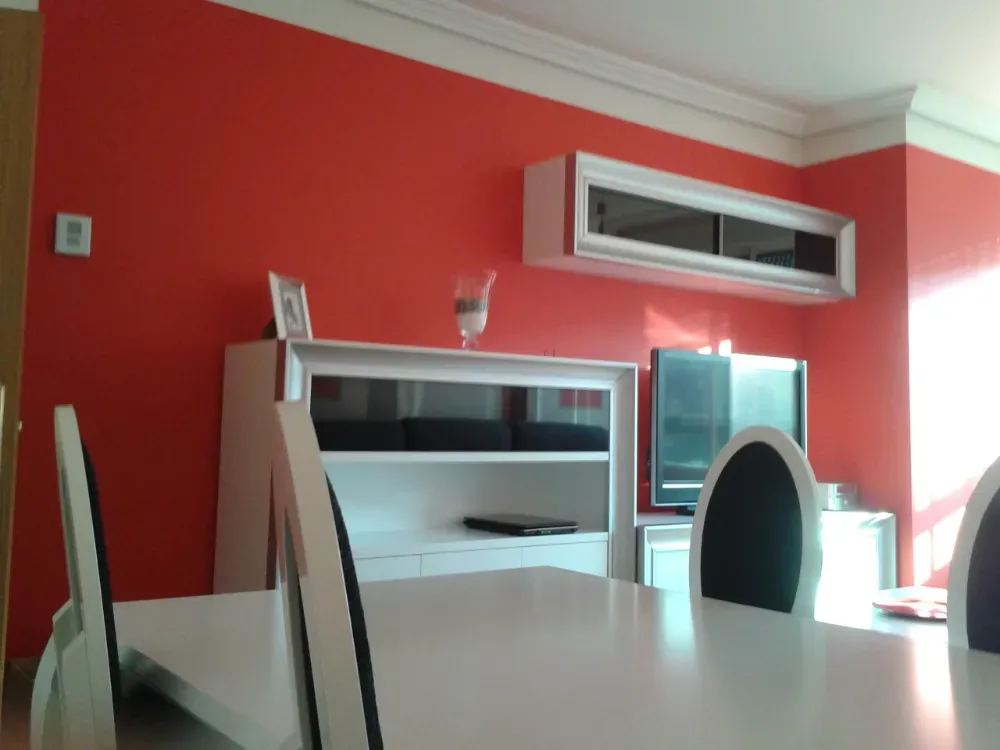 Comedor con mesa y sillas blancas, paredes rojas y mueble blanco.