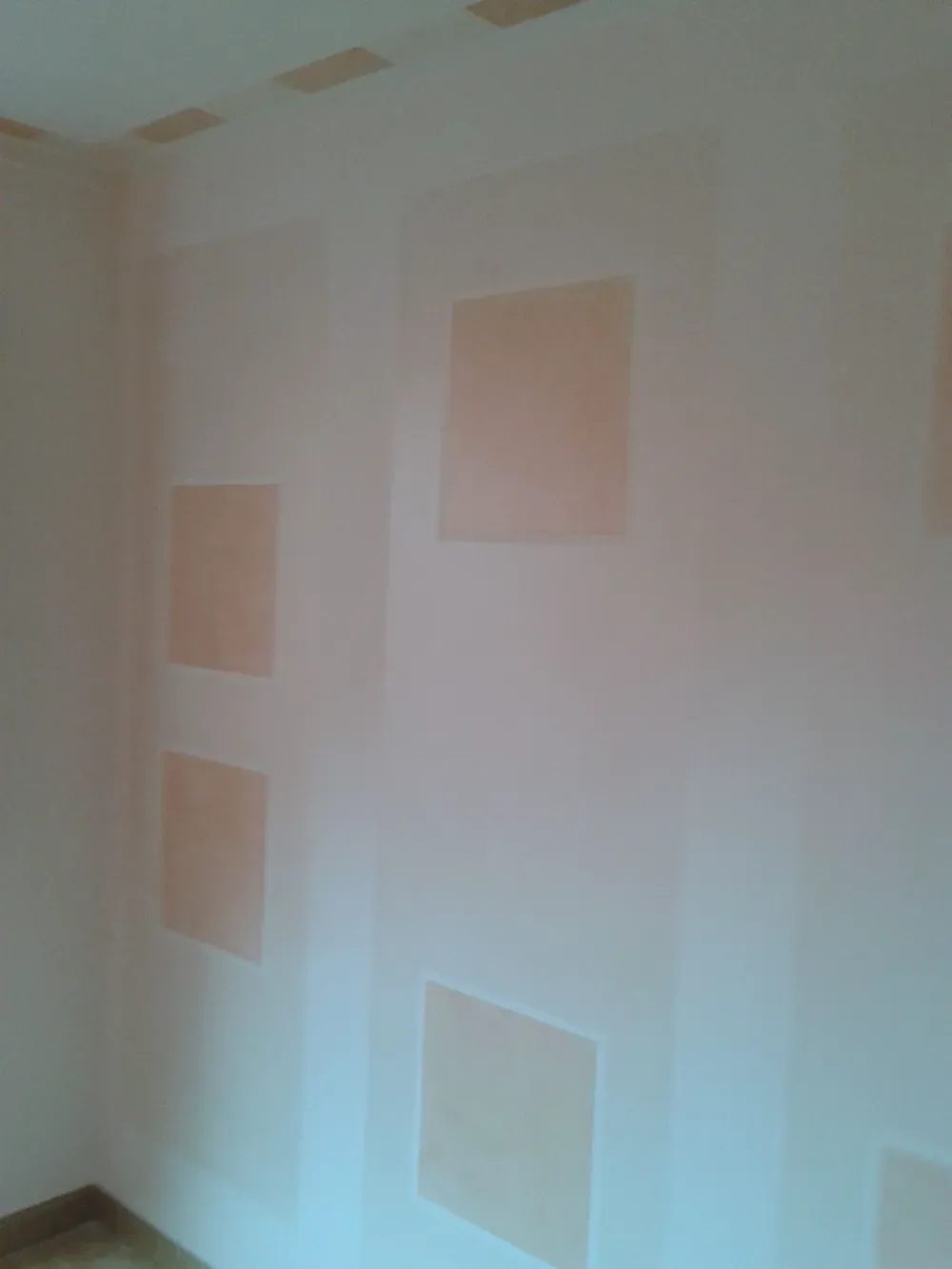 Una pared clara con cuadrados color melocotón pintados. Los cuadrados están espaciados uniformemente.