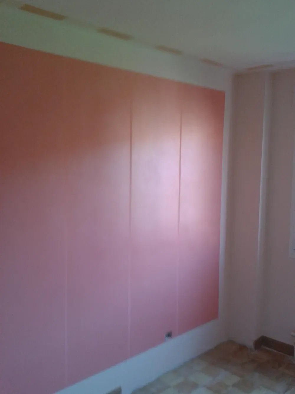 Pared con paneles de color rosa en una habitación, con molduras blancas y una pequeña pieza de herraje oscuro.