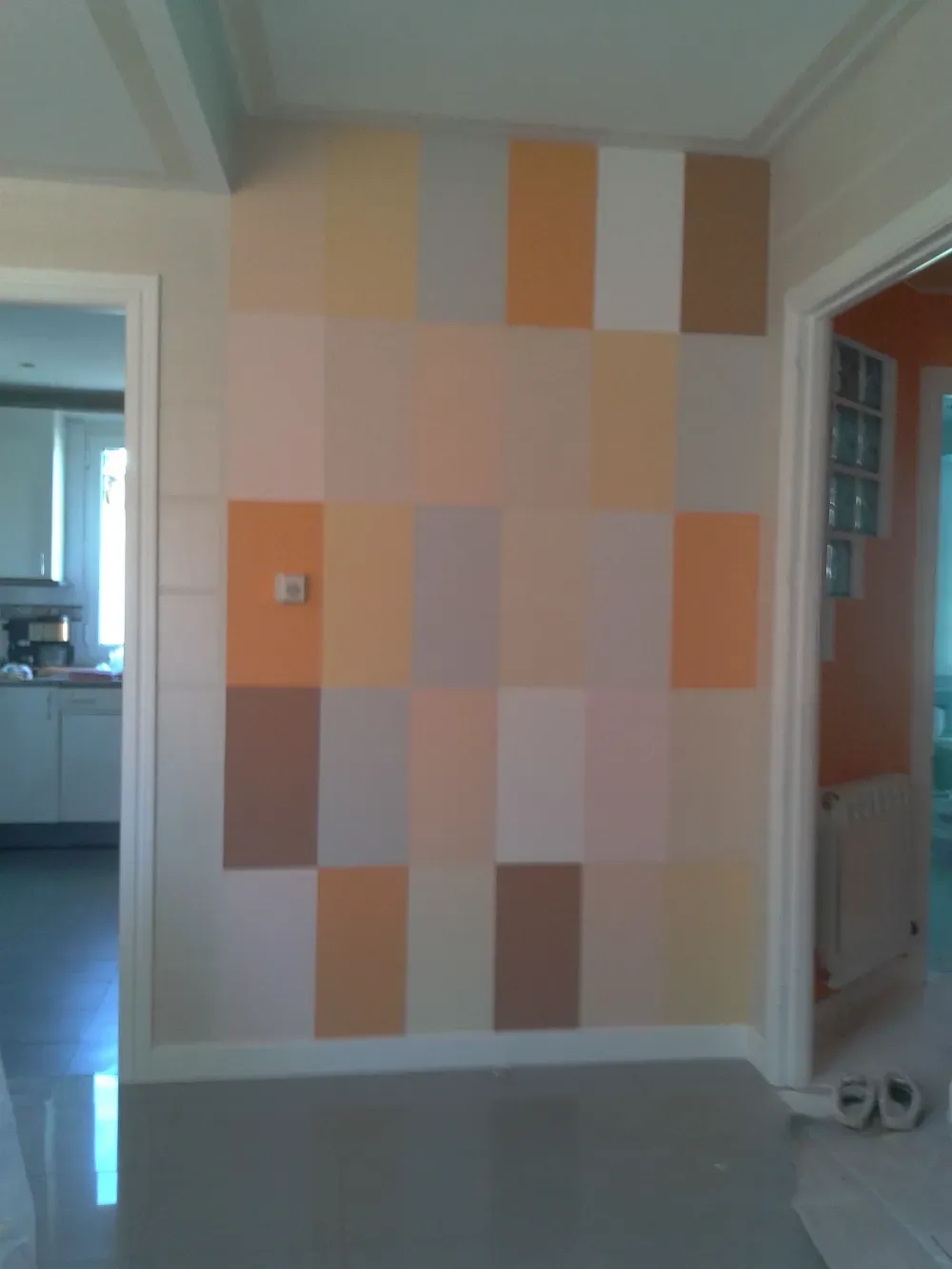 Una pared pintada con una cuadrícula de bloques rectangulares en varios tonos de naranja, tostado y gris.