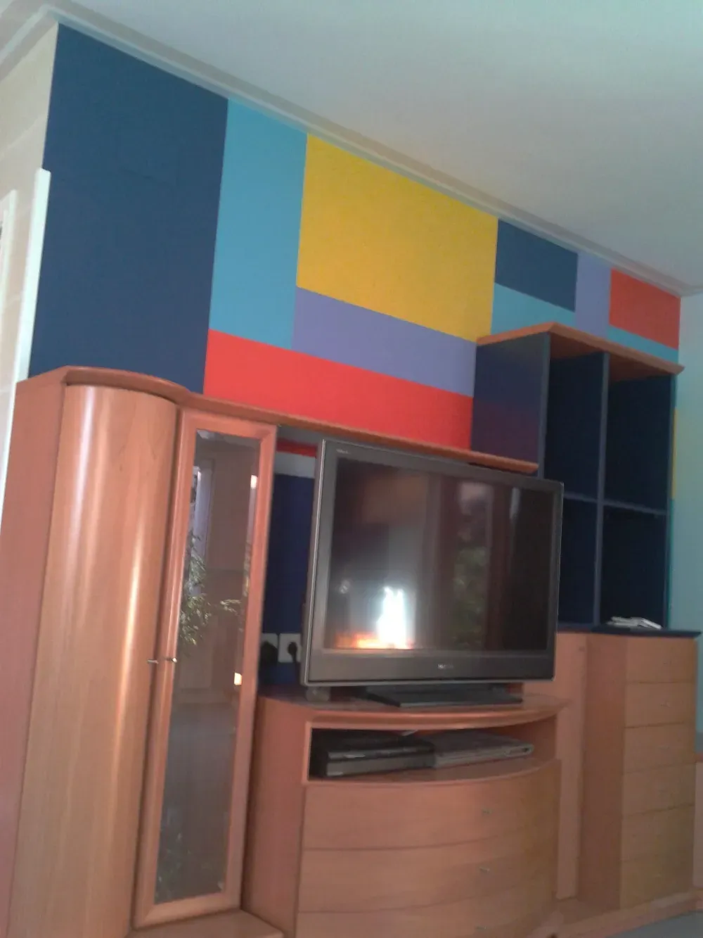 Centro de entretenimiento de madera con TV, arte de pared geométrico colorido.