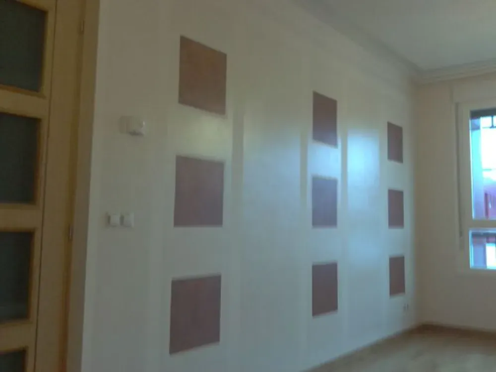 Pared interior color crema con detalles marrones rectangulares. La luz se refleja en la superficie brillante.