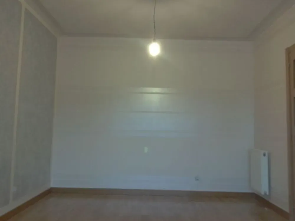 Habitación vacía con paredes blancas, una sola lámpara colgante y un radiador.