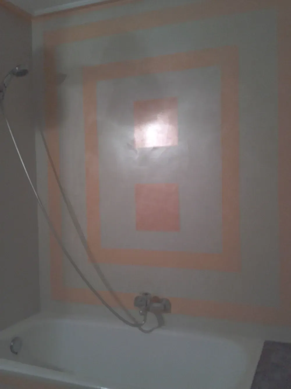 Una bañera con ducha y una pared con diseño cuadrado en color melocotón.