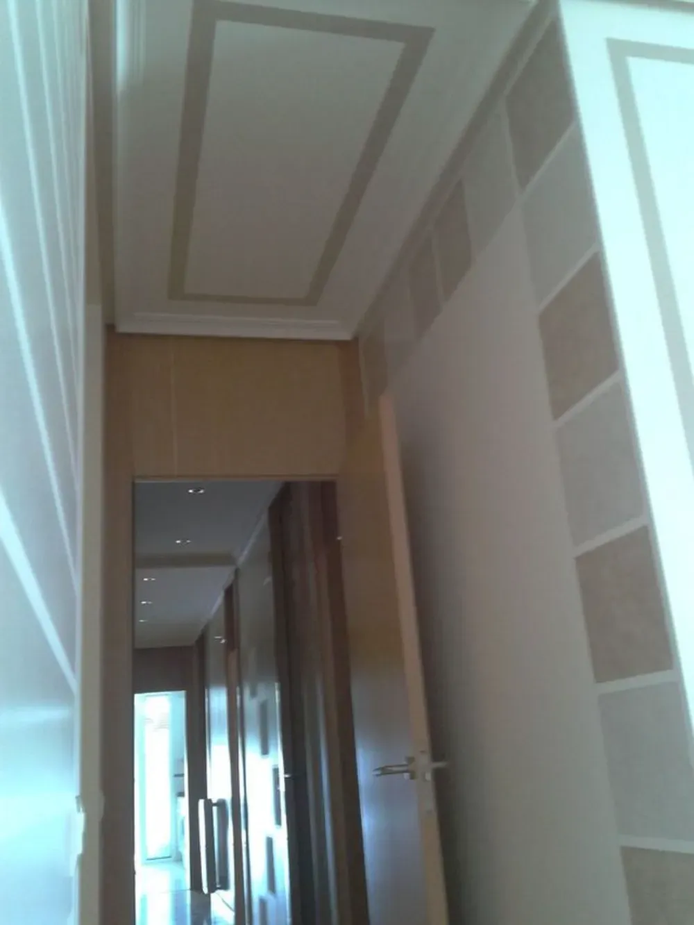 Pasillo estrecho con paredes de color beige, detalles estampados y un diseño de techo rectangular.