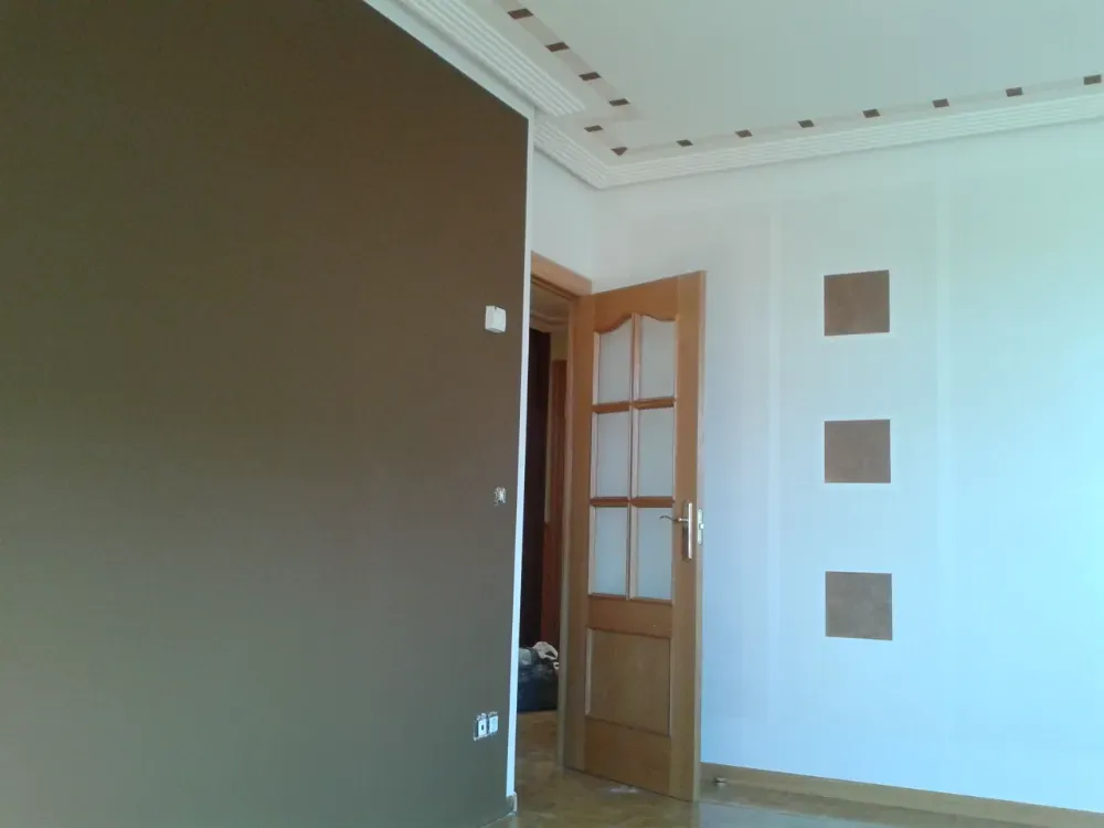 Interior de una habitación con una pared marrón, paredes blancas, puerta de madera y tres paneles cuadrados.