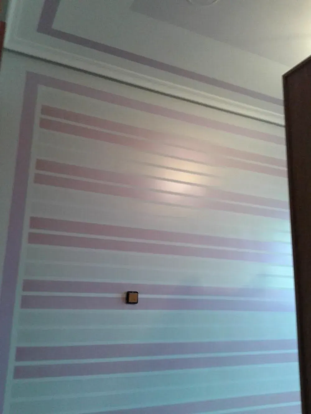 Pared blanca con rayas horizontales de color rosa, interruptor de luz cuadrado y borde de armario de color marrón.