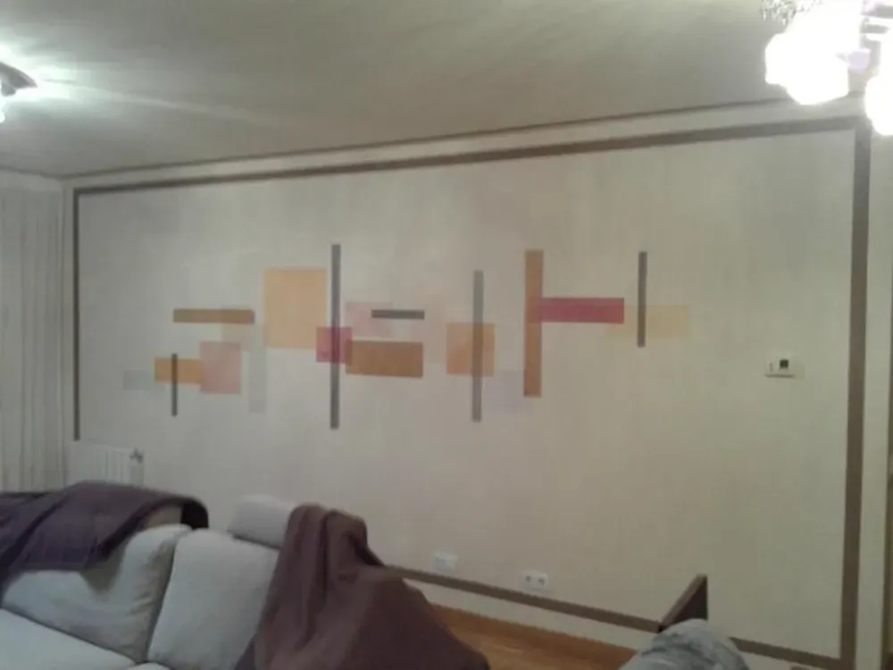 Arte geométrico abstracto sobre una pared color crema con ribete marrón. Un sofá se encuentra debajo de la obra.