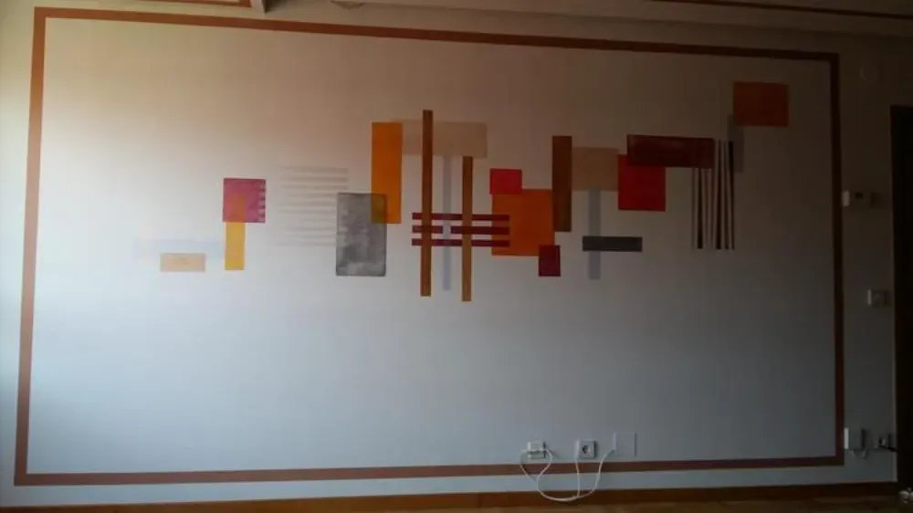 Arte de pared abstracto con formas geométricas coloridas sobre una pared blanca con borde marrón.