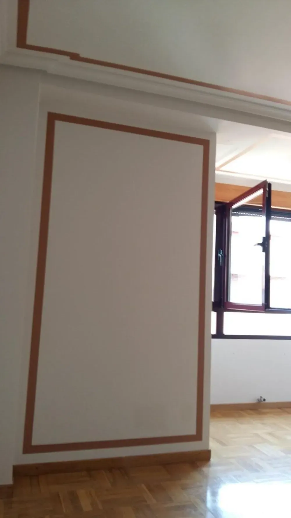 Pared interior con panel beige enmarcado por una moldura marrón. Ventana abierta al fondo.