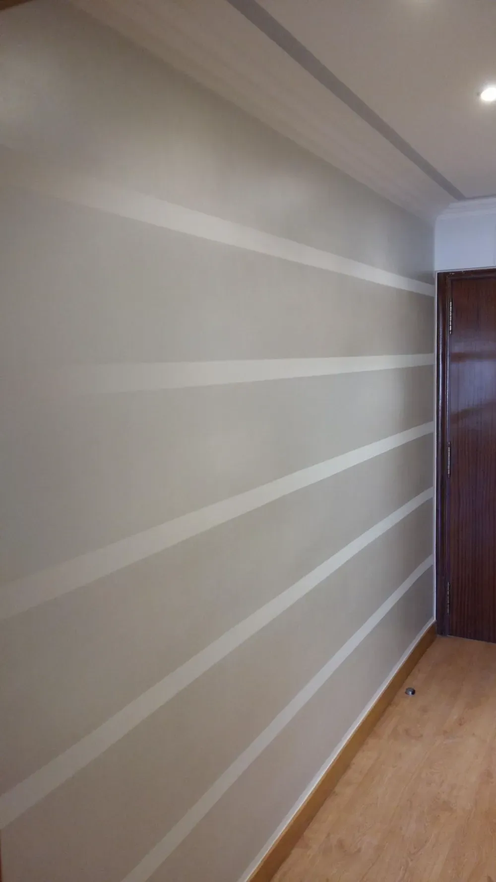 Pared gris con rayas horizontales de color claro. Puerta marrón a la derecha. Suelo de madera clara.