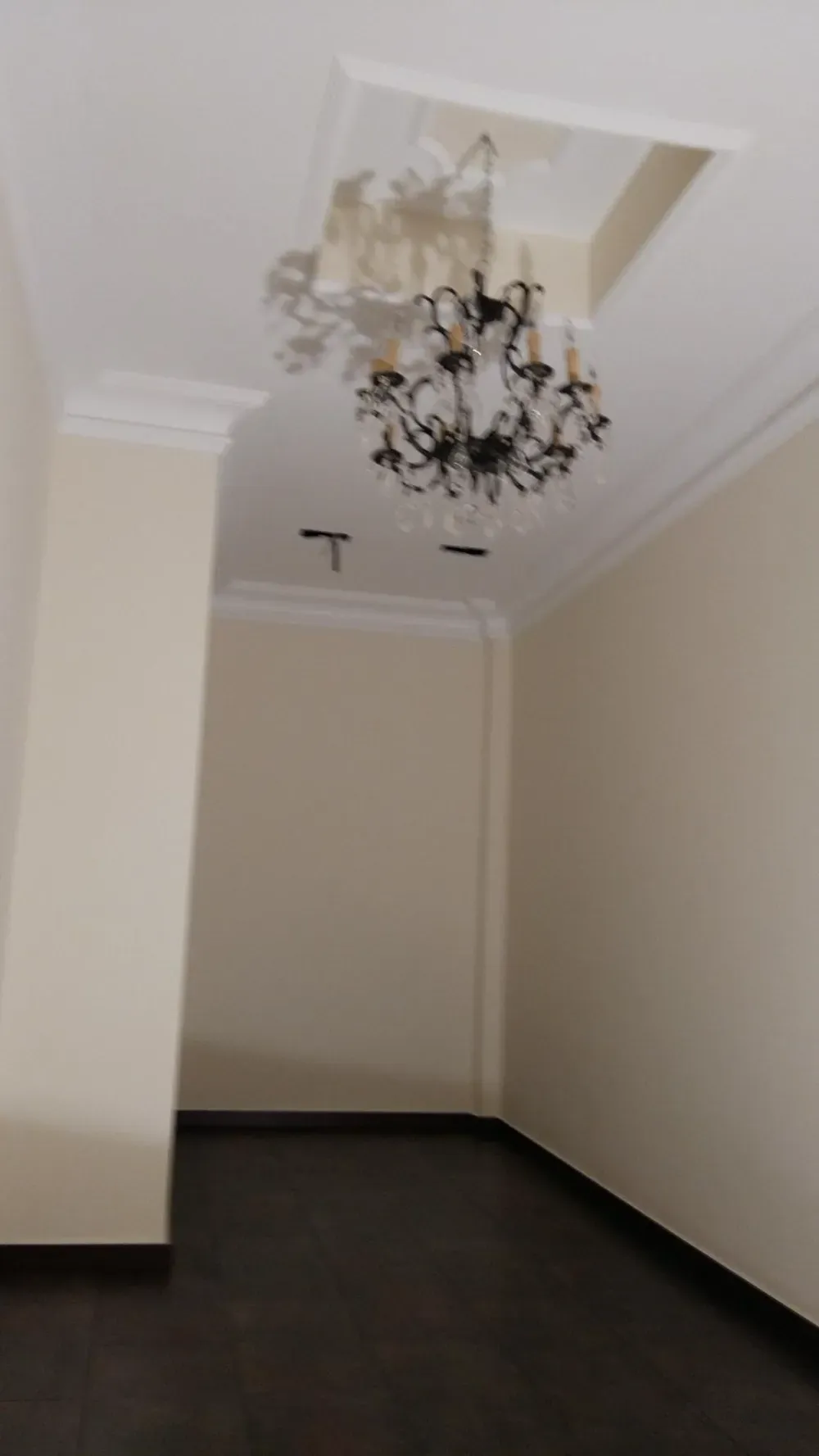 Habitación vacía con piso de madera oscura, paredes de color canela y una lámpara de araña colgando del techo.