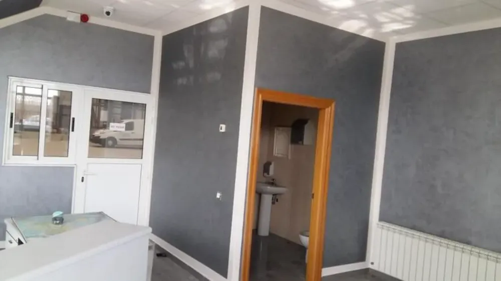 Habitación de paredes grises con molduras, puerta y ventana blancas. Incluye encimera, radiador y un pequeño lavabo.