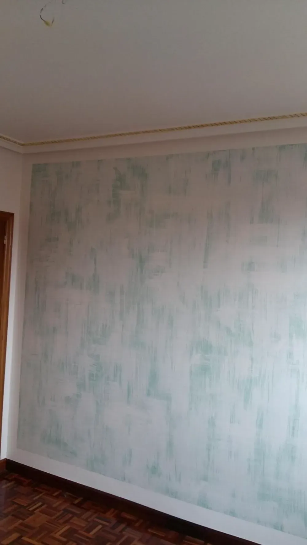 Pared blanca con vetas verdes, molduras de corona y piso de madera.