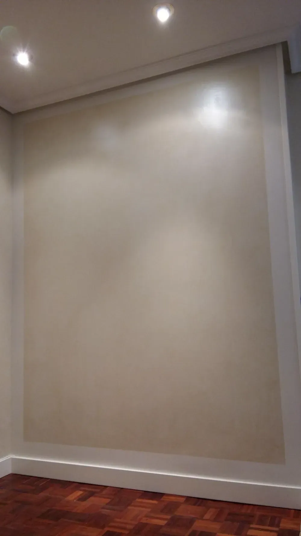 Pared beige con focos brillantes, molduras blancas y piso de madera oscura.
