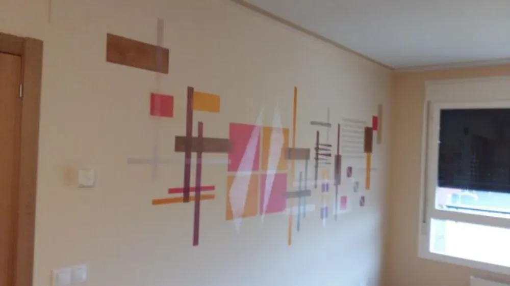 Arte de pared abstracto con formas geométricas rosas, naranjas y marrones sobre una pared de color crema