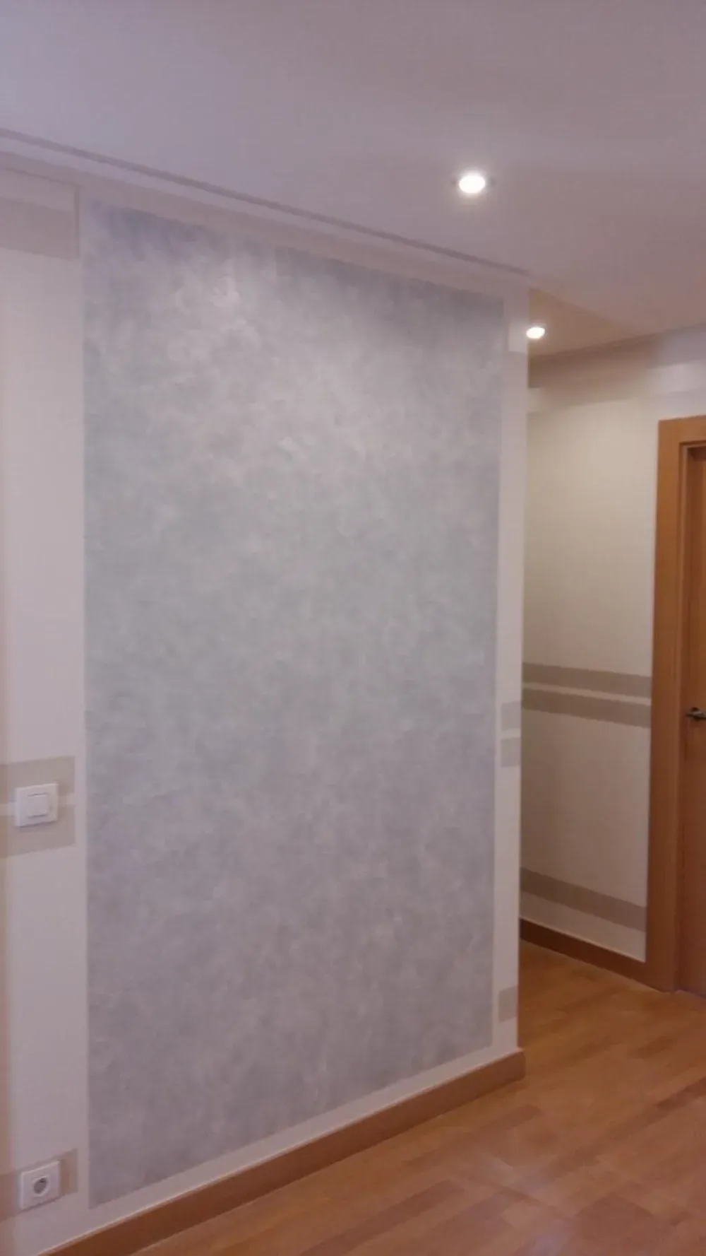 Una pared con un diseño gris texturizado. Suelo de madera, puerta y una pared circundante de color claro.