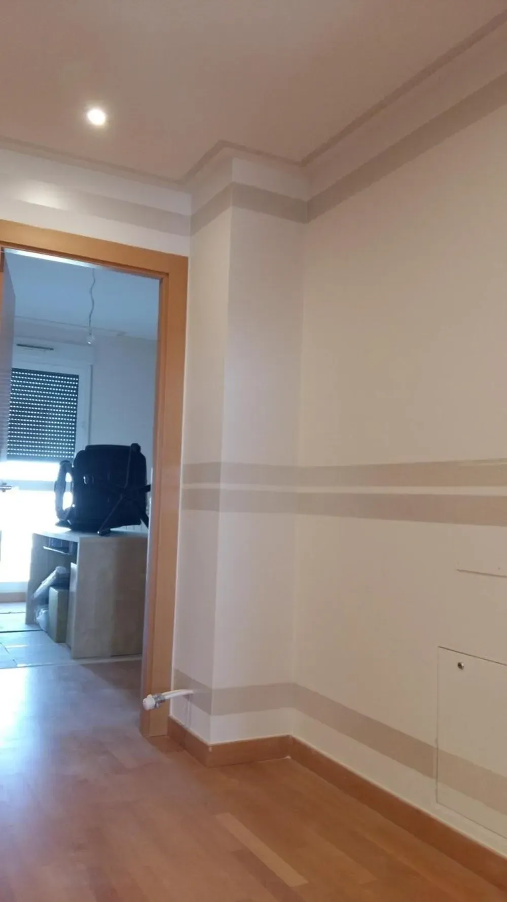 Habitación interior con paredes blancas, suelo de madera, marco de puerta y rayas decorativas beige.