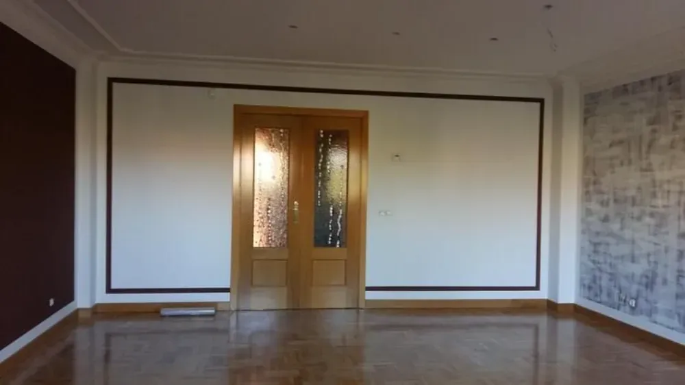 Habitación vacía con puerta de madera, paredes blancas y molduras marrones.