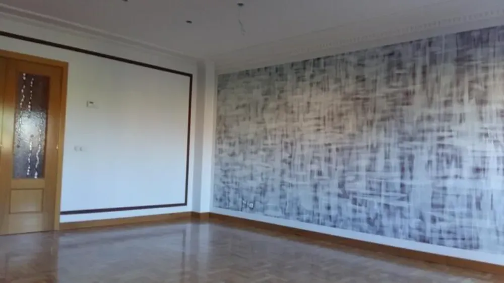 Habitación vacía con piso de madera, puerta y una pared con acento de papel tapiz texturizado.