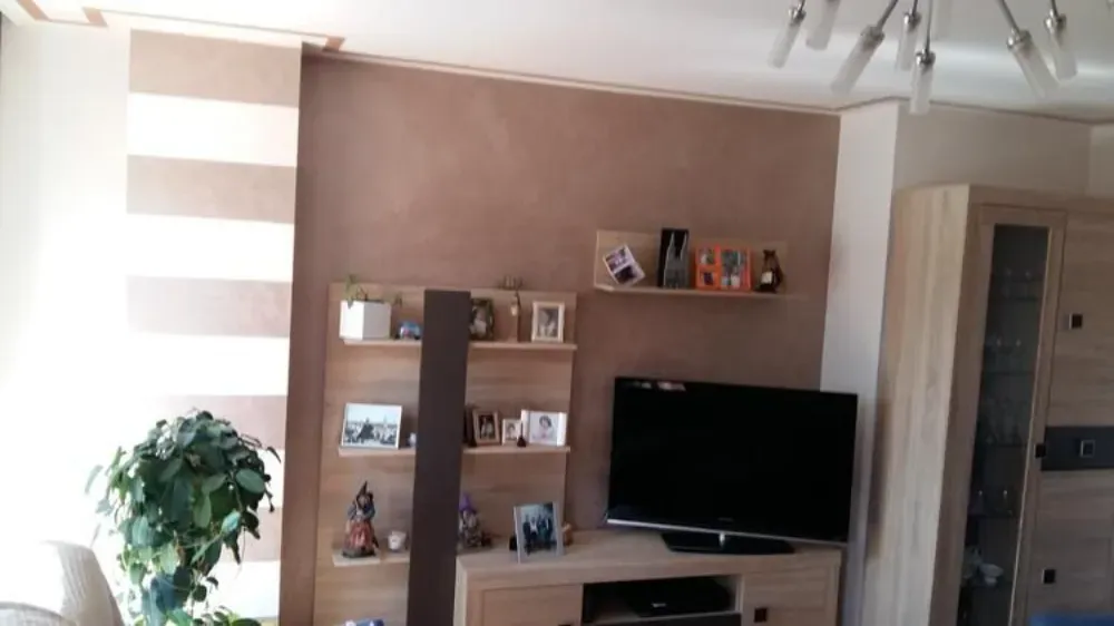 Sala de estar con TV, estanterías con fotos y decoración y una persiana a rayas.