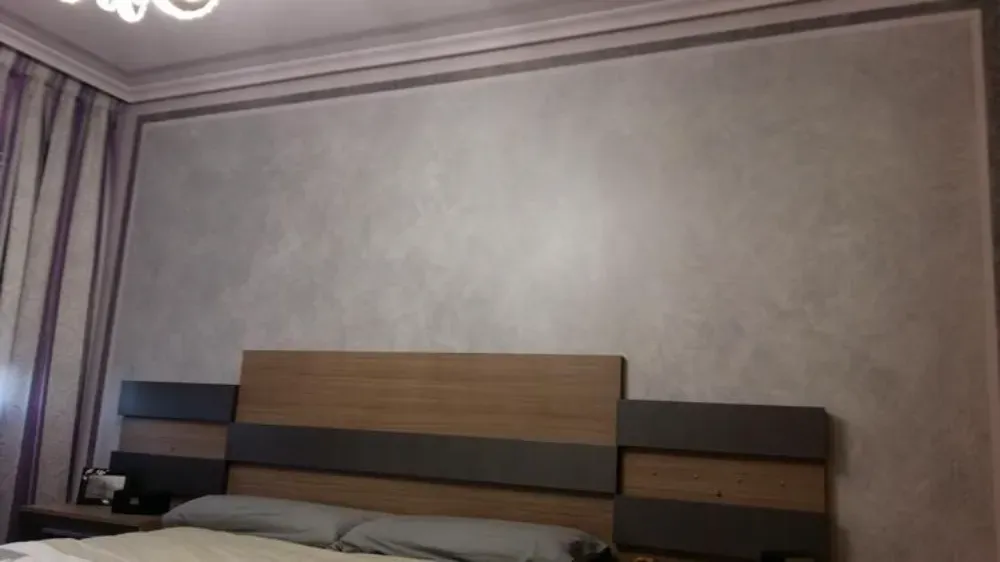 Dormitorio con cabecero, cortinas y pared gris texturizada.