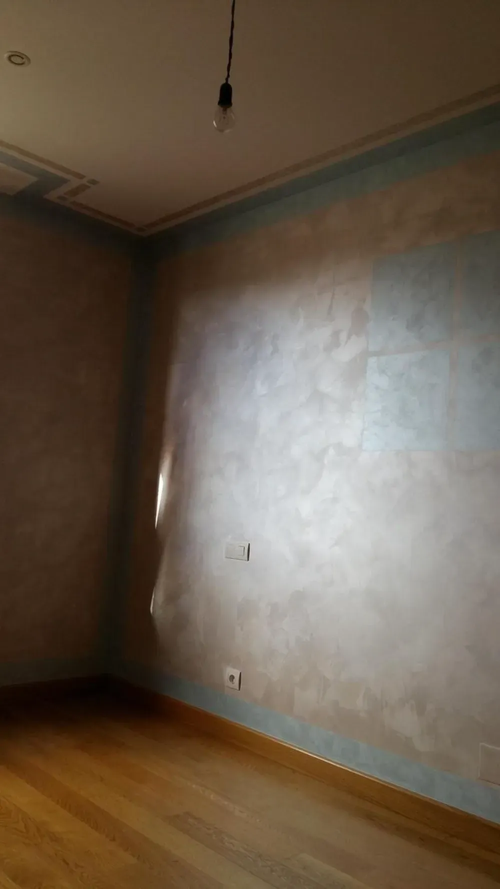 Habitación con suelo de madera, paredes texturizadas en azul y plata y bombilla a la vista.