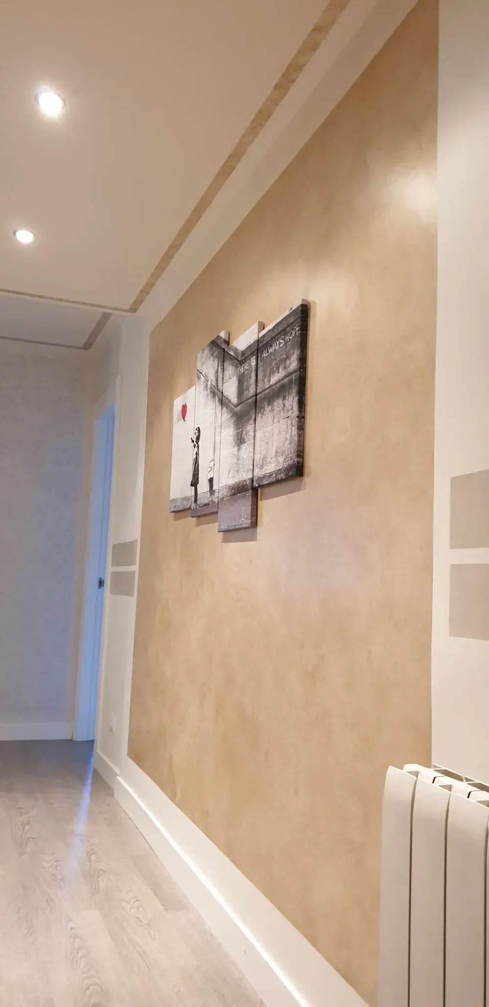 Pasillo con paredes beige, molduras blancas, obras de arte y un radiador.