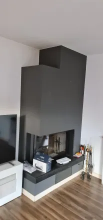 Chimenea moderna con marco gris y espacio de almacenamiento incorporado. Las paredes son blancas y el suelo es de madera.