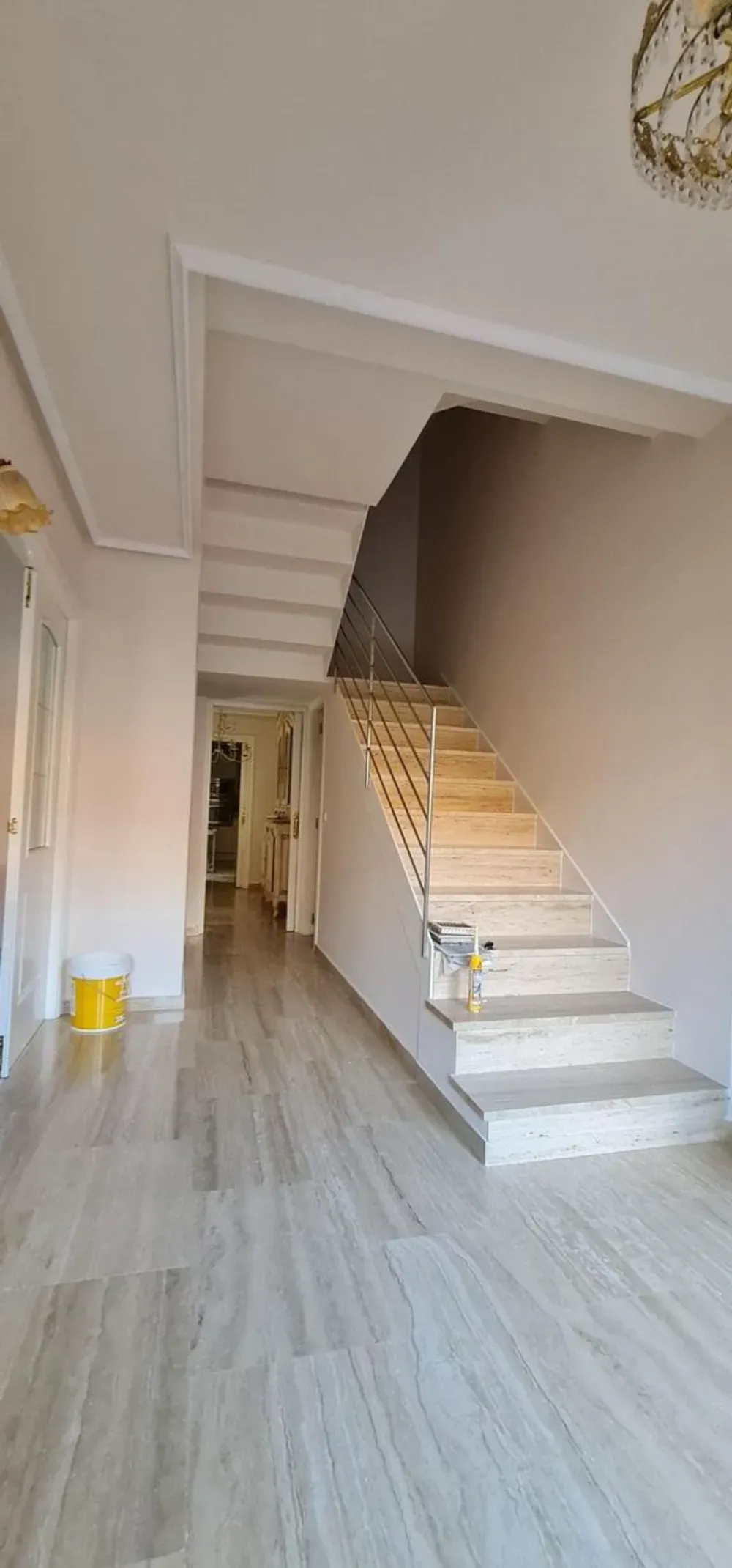 Un pasillo con suelo de mármol que da a una escalera. Un cubo amarillo en la esquina.