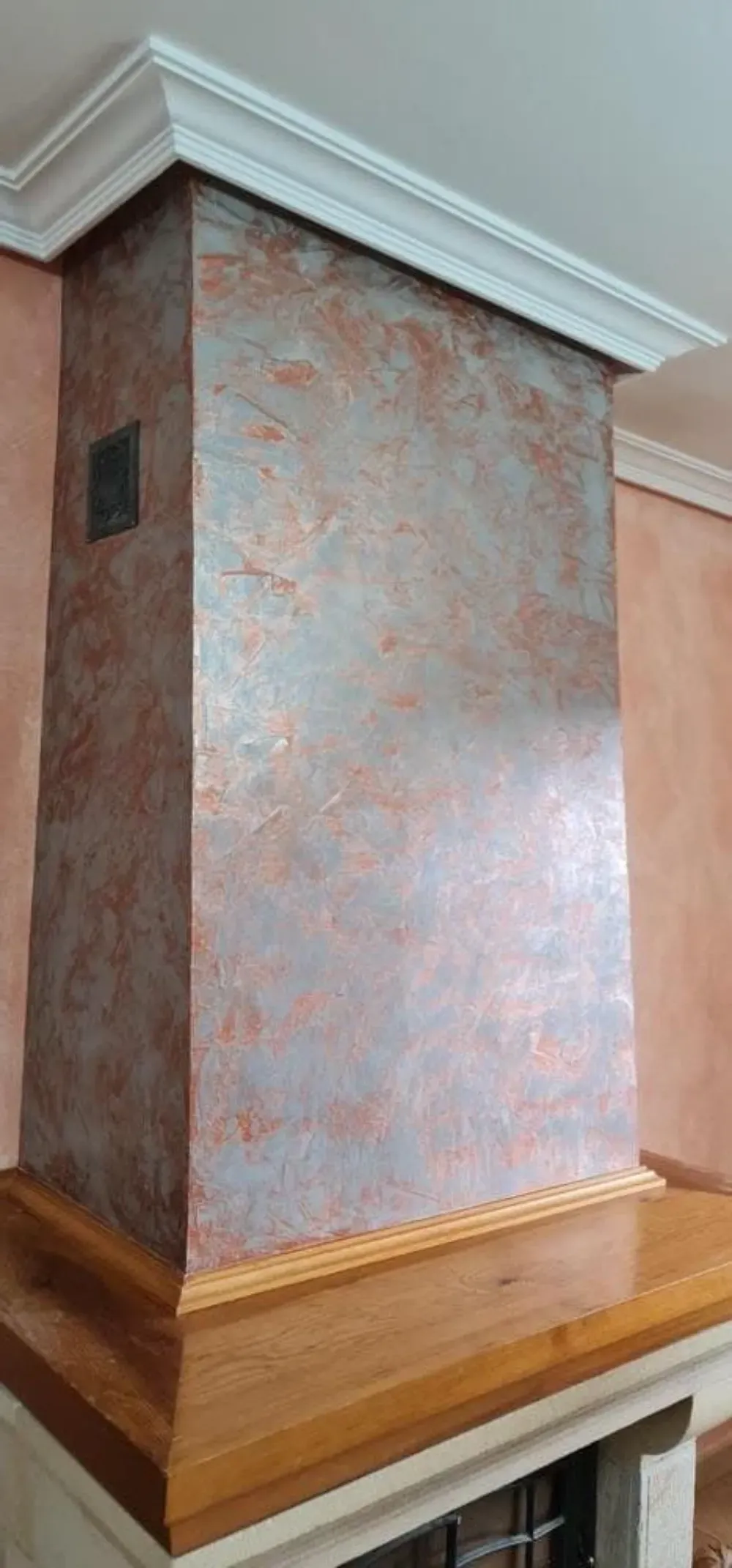 Chimenea con acabado de pared texturizado en cobre y plata, repisa de madera y moldura de corona blanca.