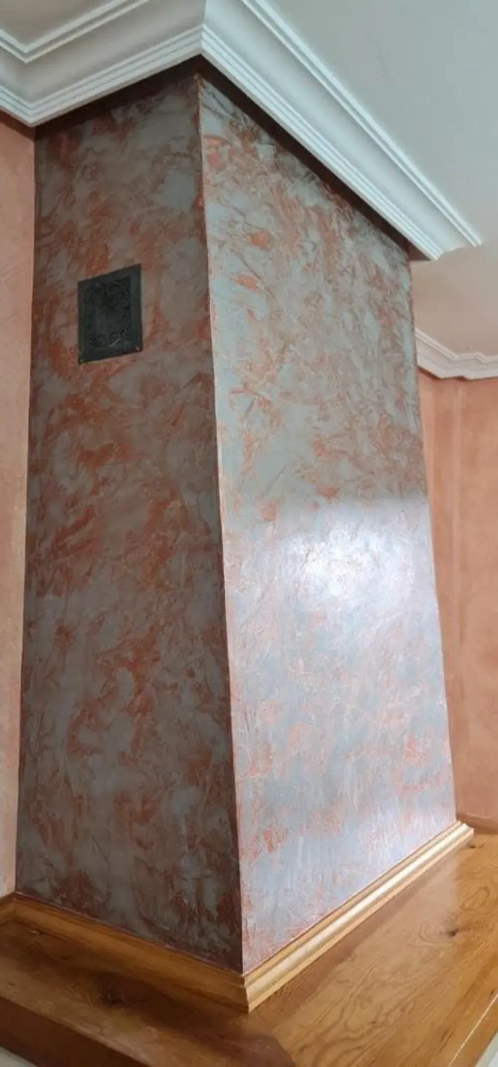 Chimenea con acabado texturizado y moteado. Cuenta con una placa metálica cuadrada. Repisa de madera y moldura de corona.