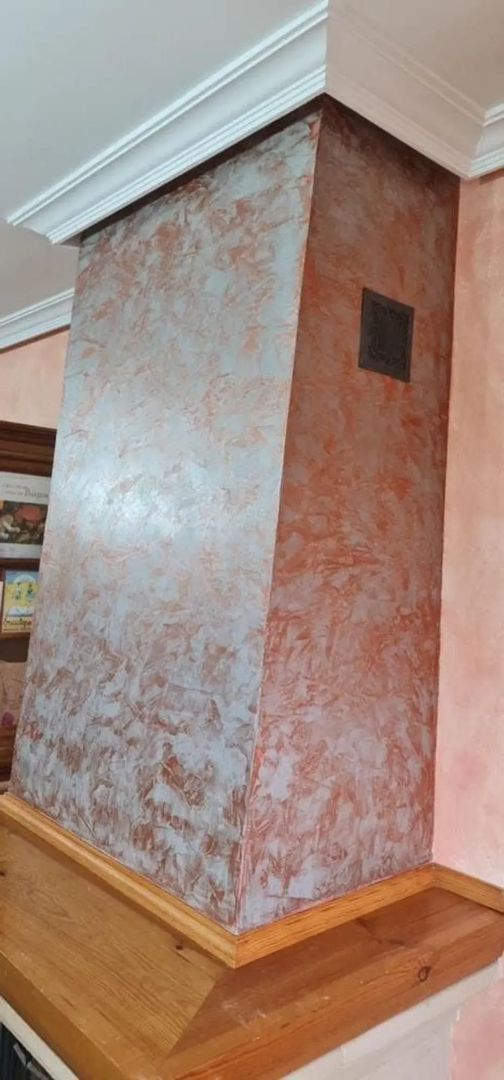 Una repisa de chimenea rústica en tonos rojos en una habitación con molduras de corona blancas.