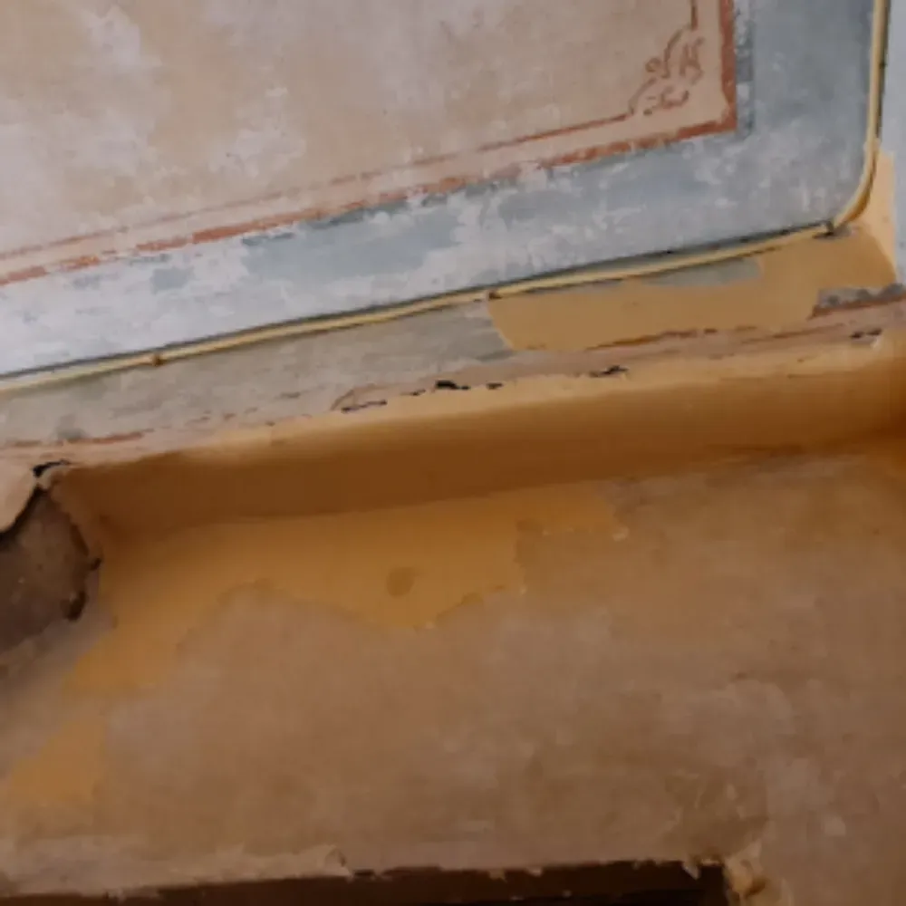 Pintura amarilla descascarada en una pared con un borde de techo decorado.