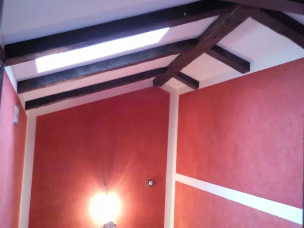 Habitación de paredes rojas con vigas de madera y tragaluz; líneas decorativas blancas, artefacto de iluminación.
