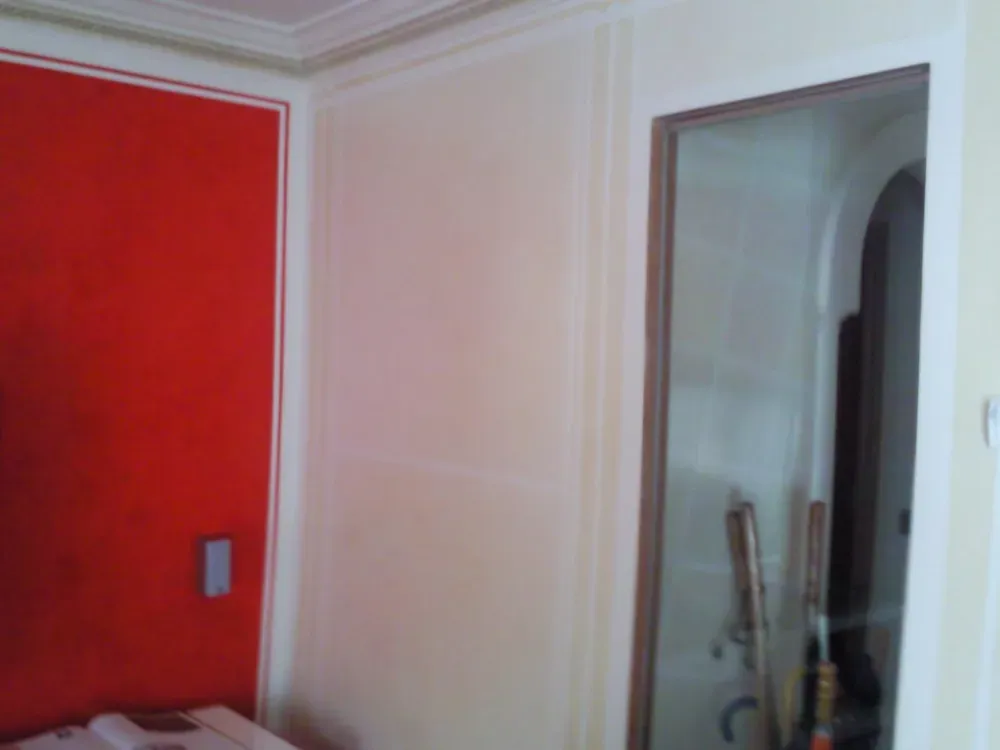 Puerta roja y pared color blanquecino con molduras, puerta a la derecha, moldura en el techo.