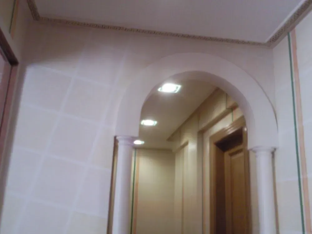 Pasillo con arco de entrada, columnas e iluminación empotrada. Paredes en tonos beige y crema.