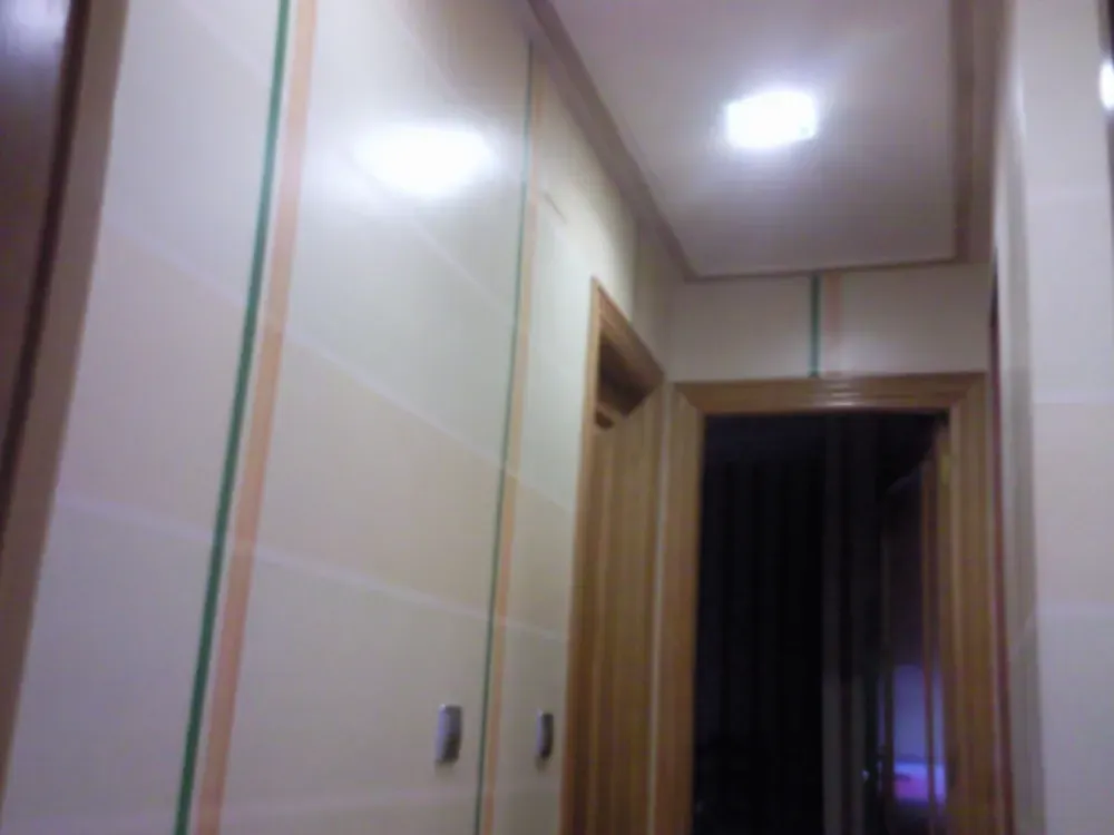 Pasillo estrecho con paredes de azulejos beige, puertas de madera e iluminación cenital.