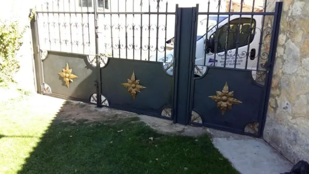 Puerta de metal adornada de color negro con detalles en forma de sol dorado, parcialmente abierta