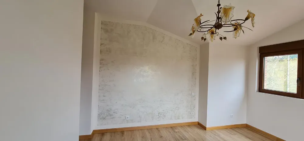 Interior de habitación con pared texturizada, piso de madera, ventana y lámpara de araña.