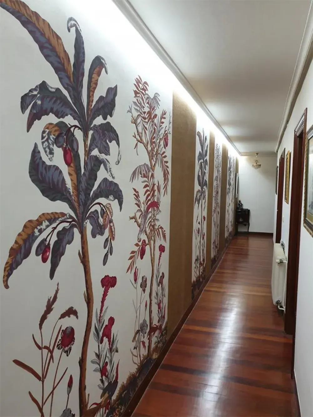 Pasillo con papel pintado floral a la izquierda, suelo de madera y cuadros a la derecha.
