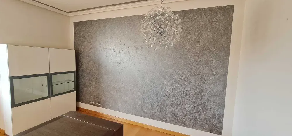 Interior de dormitorio con una pared con acento texturizado gris, una lámpara de araña y un armario blanco.