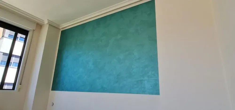 Una habitación con una pared verde azulado, molduras de corona y una ventana. Las paredes adyacentes son blancas.