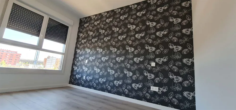 Habitación interior con una pared de papel tapiz estampado, ventana y suelo gris.