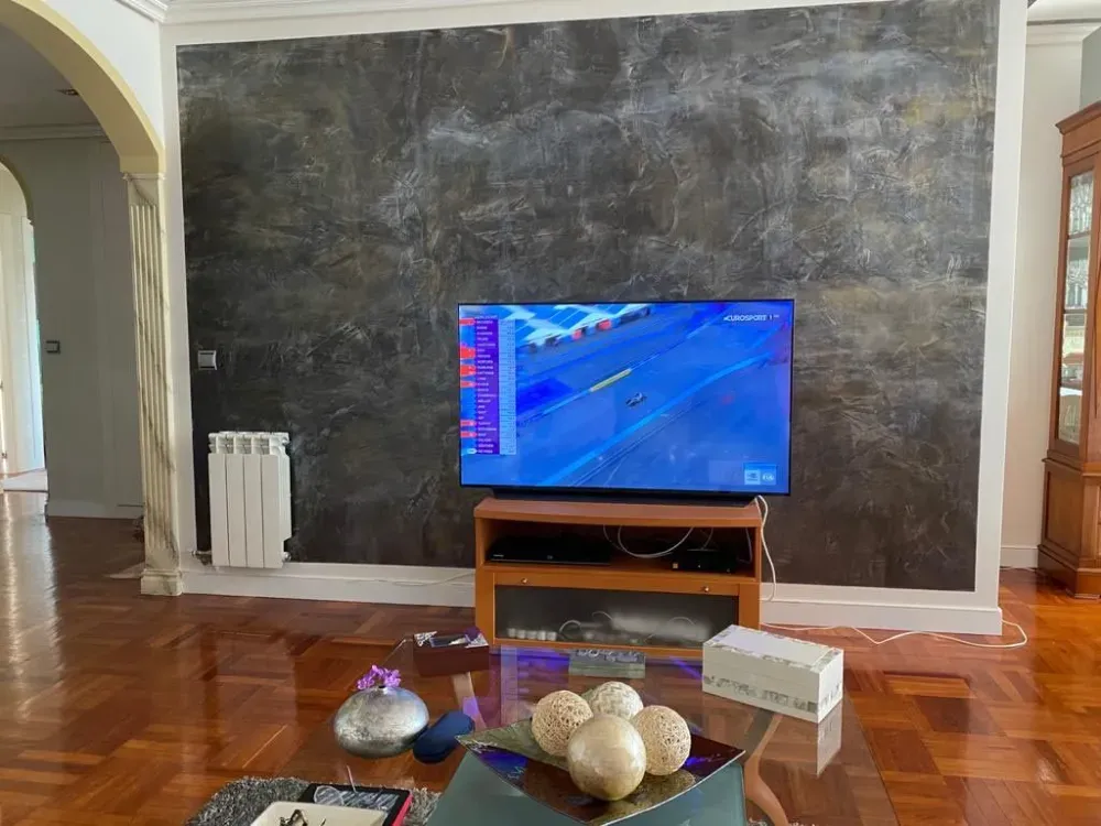 Sala de estar con televisor que reproduce un video de carreras en tonos azules, pared con textura oscura,