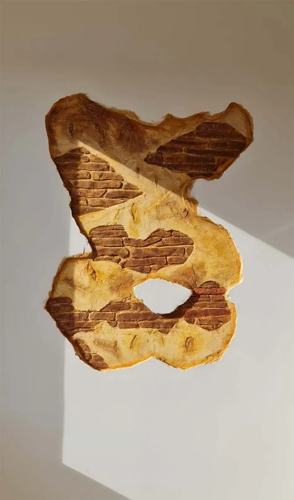 Agujero en una pared que revela un interior de ladrillo, rodeado de pintura beige descascarada e iluminado por una sombra.