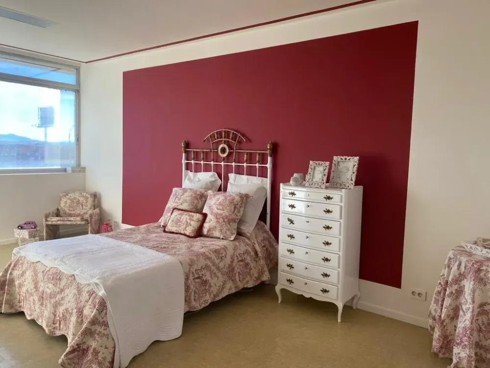 Dormitorio con pared con acento rojo, muebles blancos, ropa de cama floral y ventana.