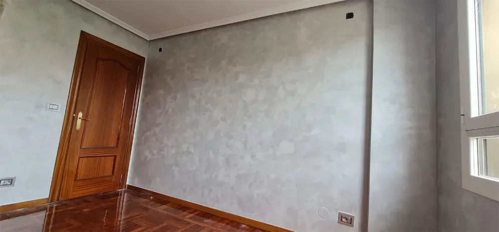 Interior de una habitación con puerta marrón, paredes grises y piso de madera.