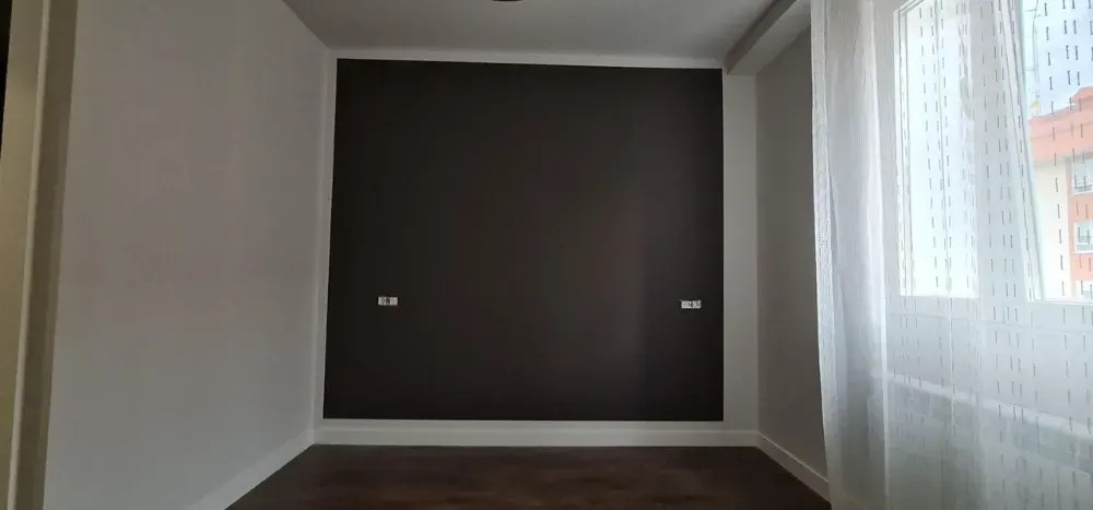 Habitación vacía con una pared marrón oscuro. Paredes blancas, suelo de madera y una cortina transparente.